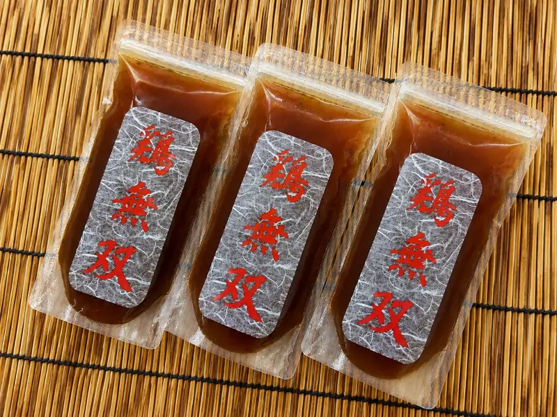鶏無双スープ。竹のマットに並んだ、鶏無双のラベルが付いた袋入りスープ3本。