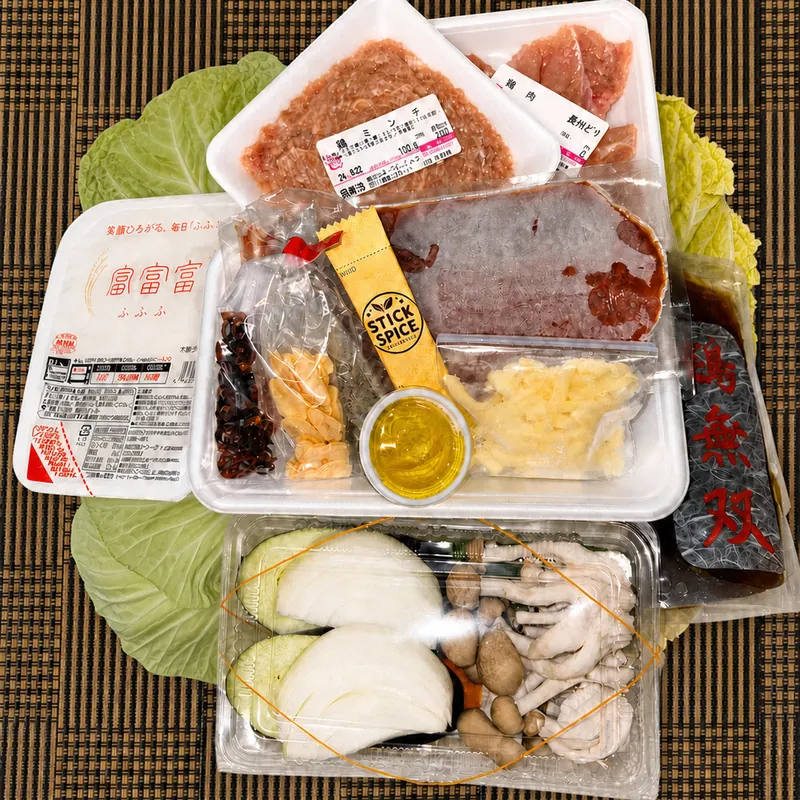 トマト鍋セット一式。ござの上に敷いたキャベツと白菜に、トマトスープ、鍋ミンチ、鍋肉（長州どり）、カット野菜、チーズ、〆のリゾットセットを並べたところ。